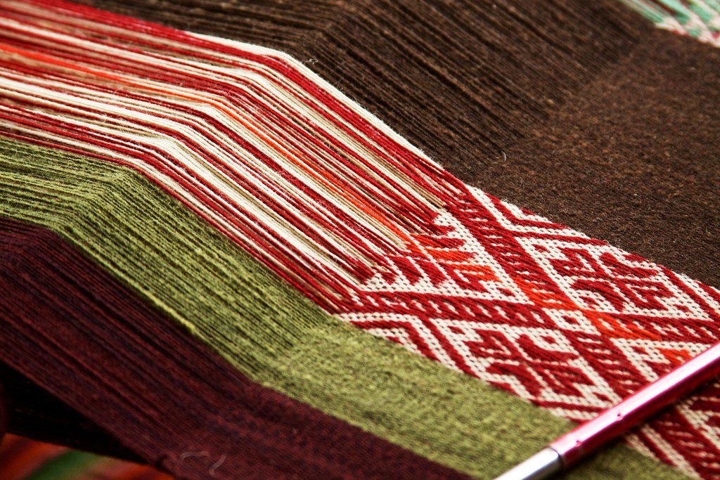 Artesana peruana tejiendo en telar tradicional, hilos de colores cálidos
