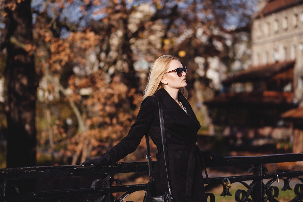 Mujer con abrigo oscuro y gafas de sol en un puente, luz de otoño