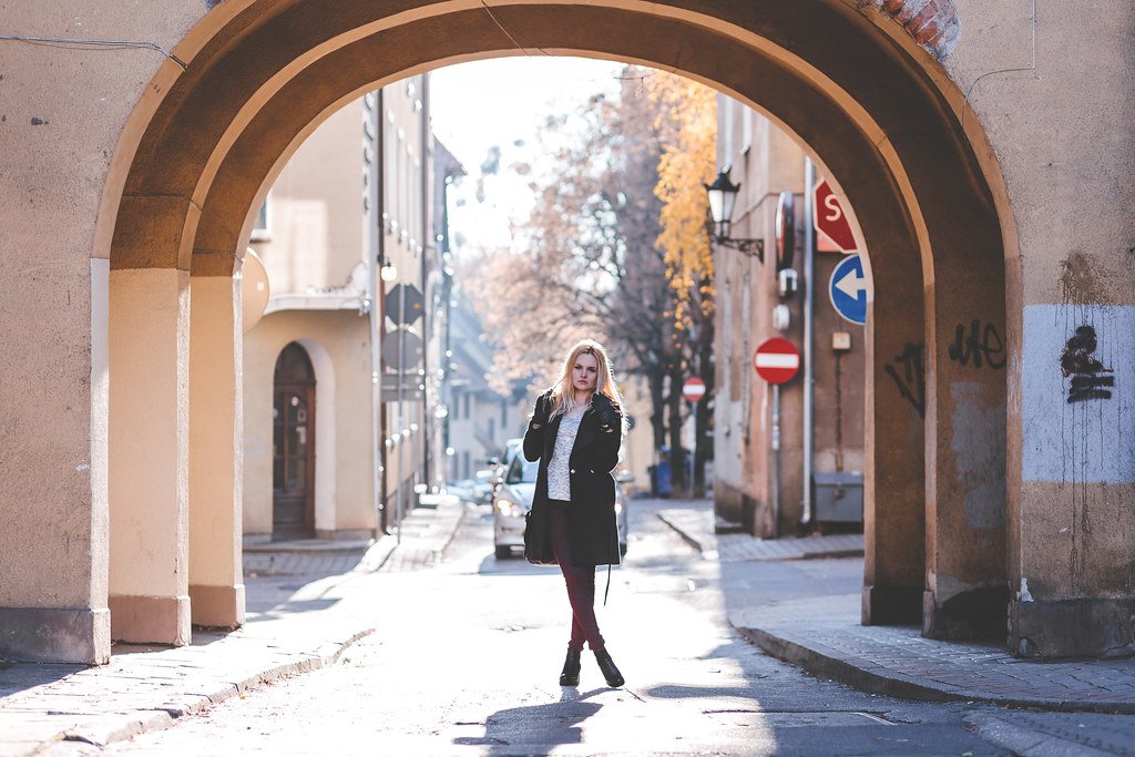 Mujer caminando bajo un arco de piedra en una calle europea