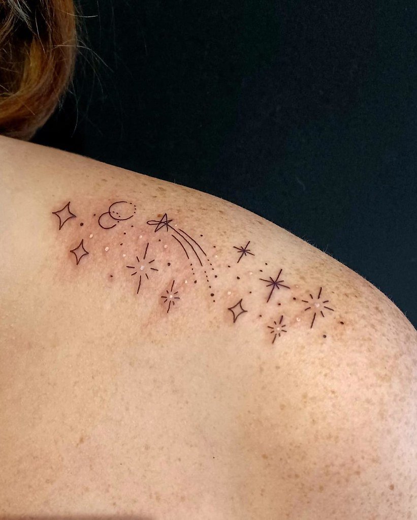 Constelación y estrella fugaz de trazo fino tatuadas sobre el hombro, fondo oscuro